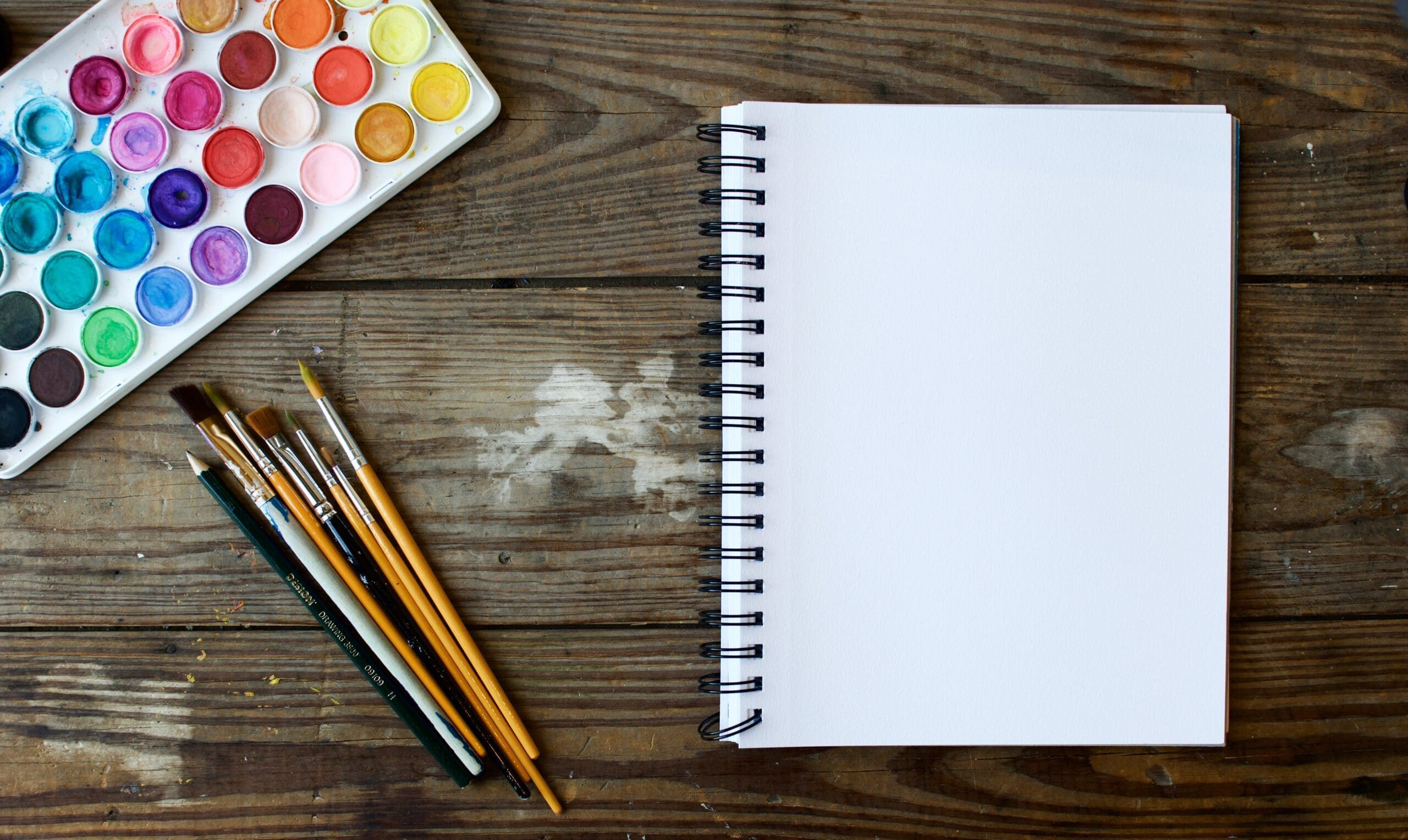 Paint pallett on a desk with paint brushes and an art book